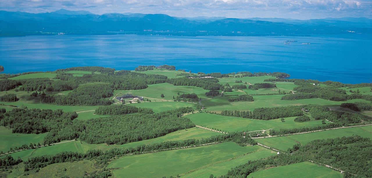 Aerial with fields, forests, lake, mountains, and sky