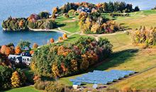 aerial view of solar panels in field with coach barn, inn, lake in foliage season