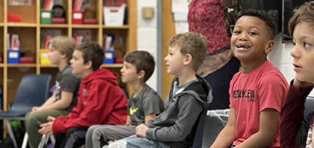 A classroom of young students sitting in a circle watch a Dairy in the Classroom lesson. One student smiles at camera.