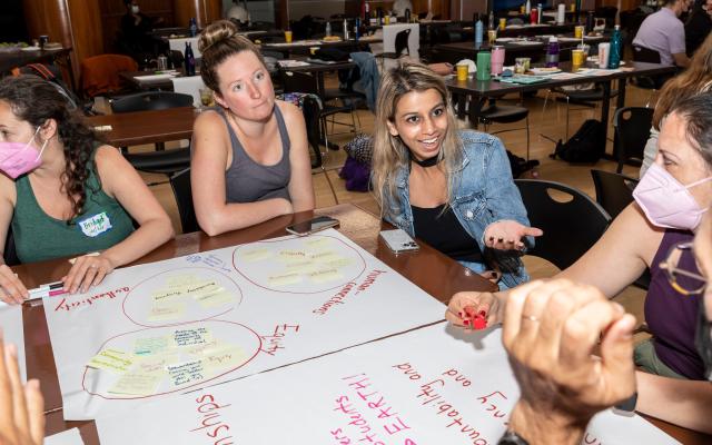 Teachers gather around a table covered in markers and colorful posters at the Coach Barn.