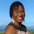 Educator Peju Okungbowa smiles at Shelburne Farms. The Adirondack mountains are in the distance with a blue sky above.